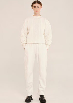 Person wearing a white outfit with black shoes on a light gray background