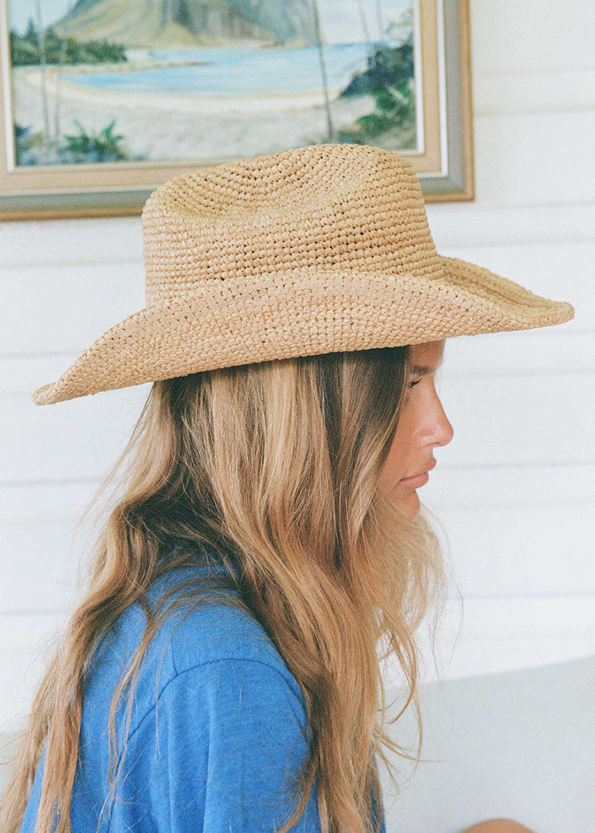 Person wearing a straw hat with a scenic painting in the background