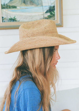 Person wearing a straw hat with a scenic painting in the background