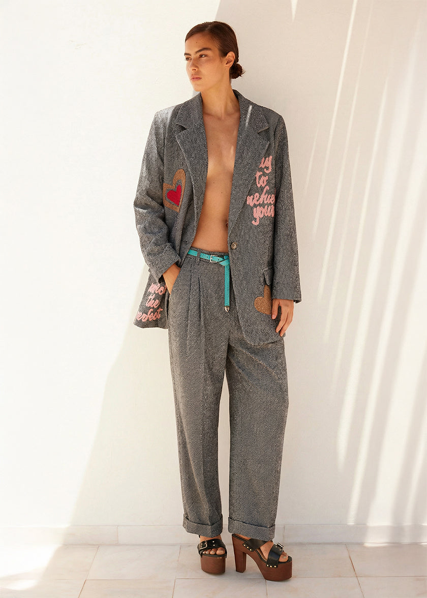 Person wearing a gray suit with a heart design, standing against a white curtain.