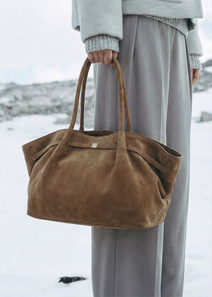 Brown suede handbag held by a person in a snowy landscape