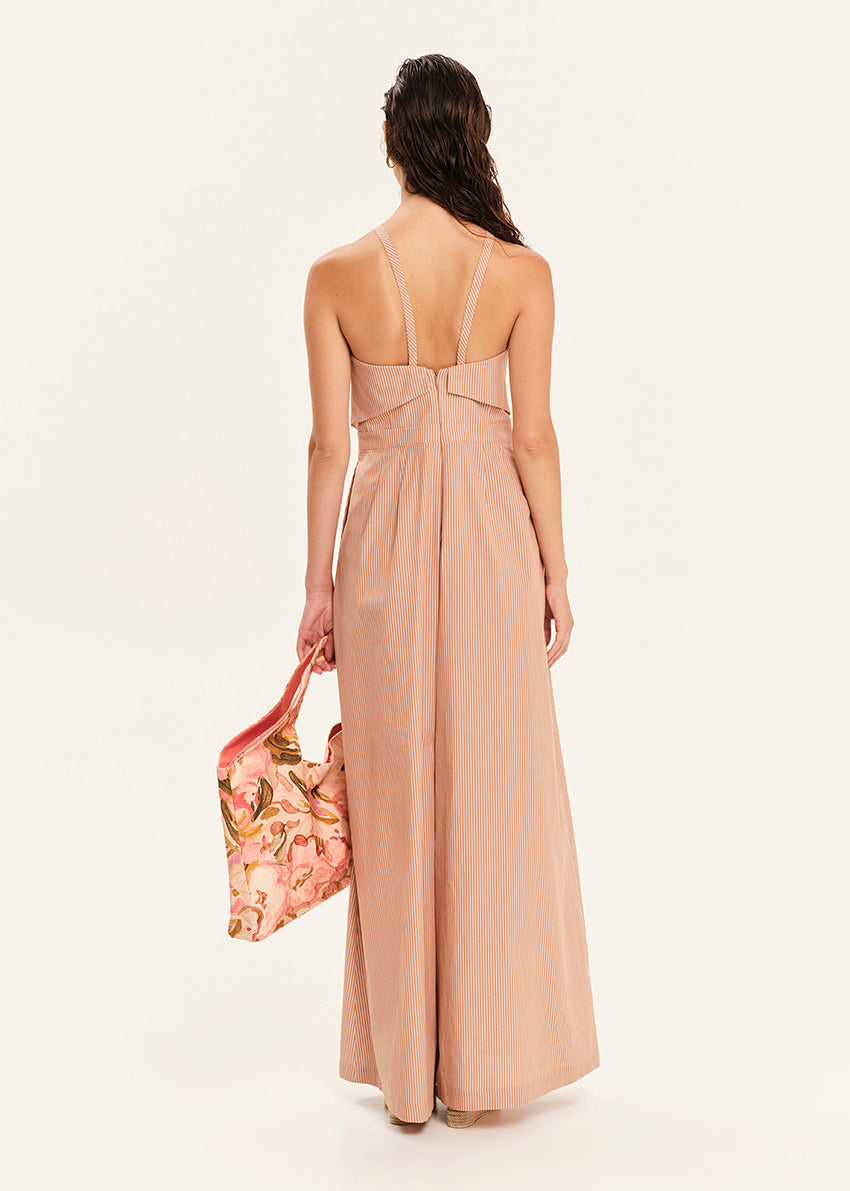 Woman wearing a beige jumpsuit holding a floral bag on a white background