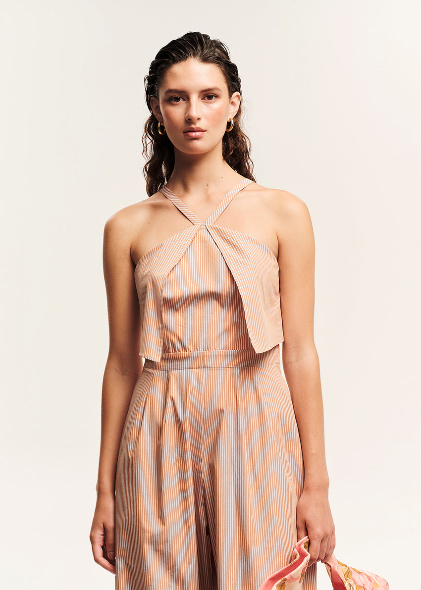 Woman wearing a beige jumpsuit holding a floral handbag on a white background