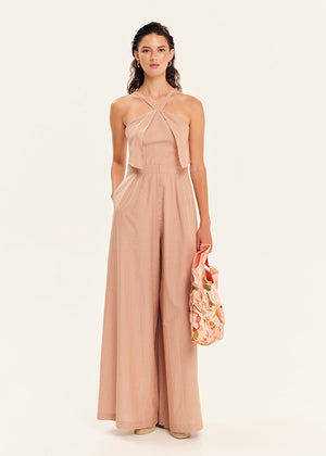 Woman wearing a beige jumpsuit holding a floral handbag on a white background