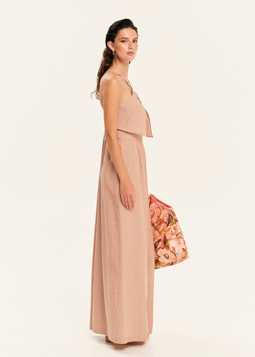 Woman wearing a beige jumpsuit holding a floral bag on a white background