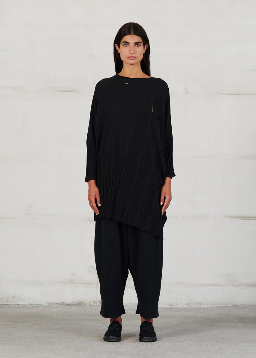 A long-sleeved, asymmetrical, knitted beige blouse with grunge details, displayed on a hanger.