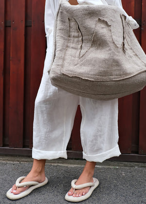 Person wearing a beige textured bag and white pants against a red wooden background