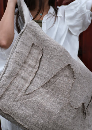 Close-up of a textured gray bag with a person wearing a white shirt in the background.