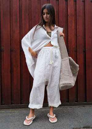 Woman in a white outfit with a beige cardigan standing against a red wooden fence.
