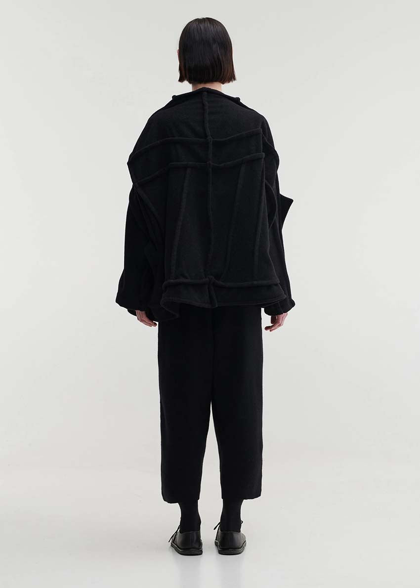 A model wearing an oversized black wool blend jacket with large front pockets, a high neckline, and long sleeves.