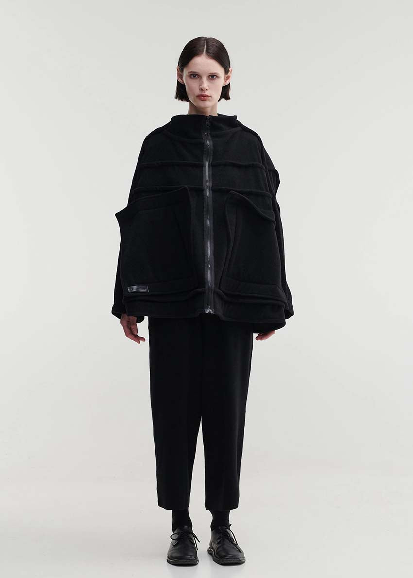 A model wearing an oversized black wool blend jacket with large front pockets, a high neckline, and long sleeves.