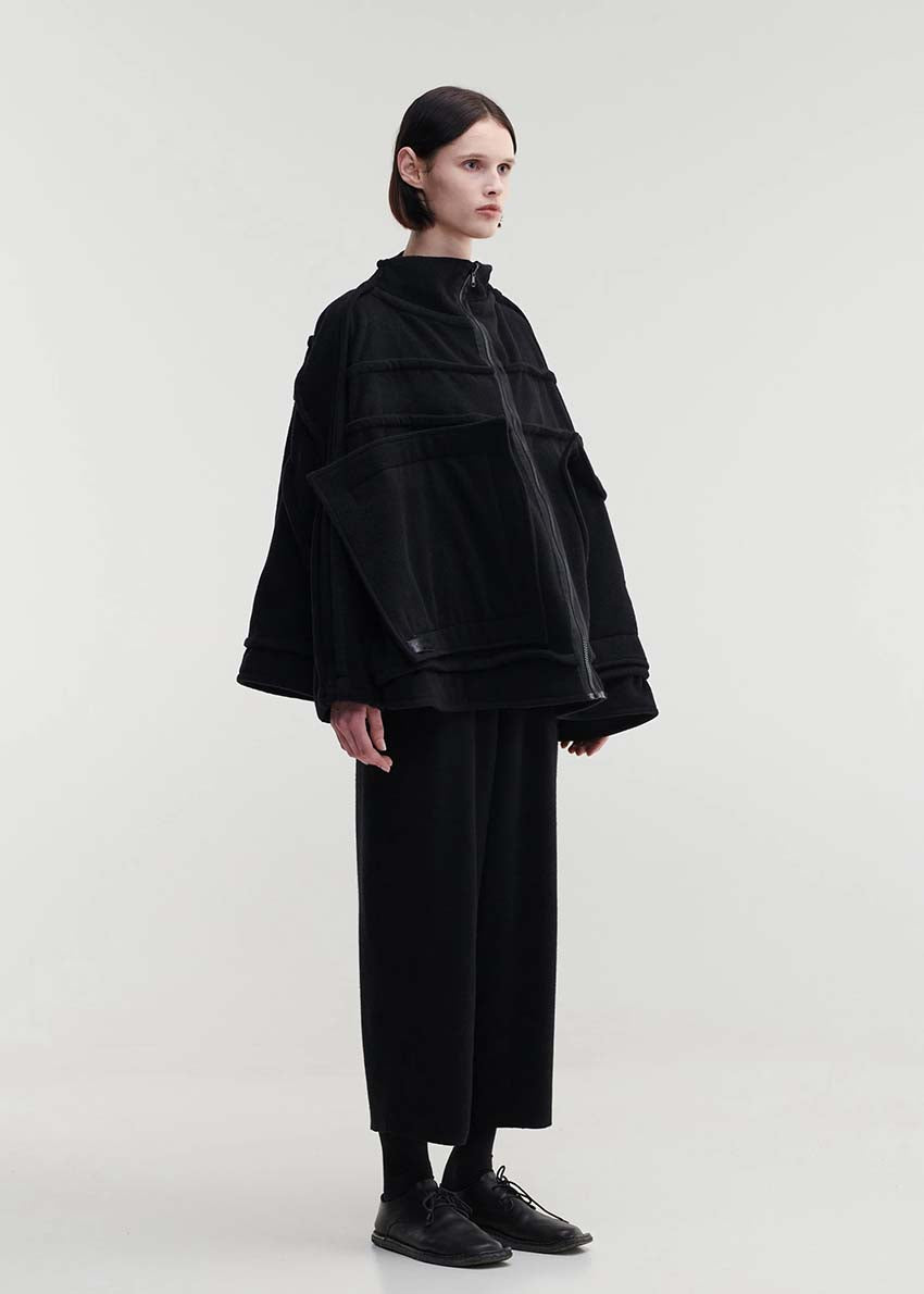 A model wearing an oversized black wool blend jacket with large front pockets, a high neckline, and long sleeves.