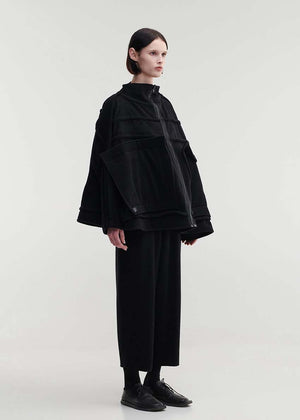 A model wearing an oversized black wool blend jacket with large front pockets, a high neckline, and long sleeves.