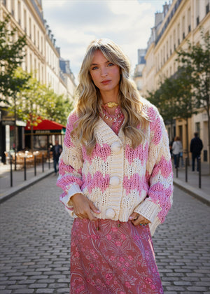 Woman wearing a pink and white patterned cardigan and skirt on a city street.
