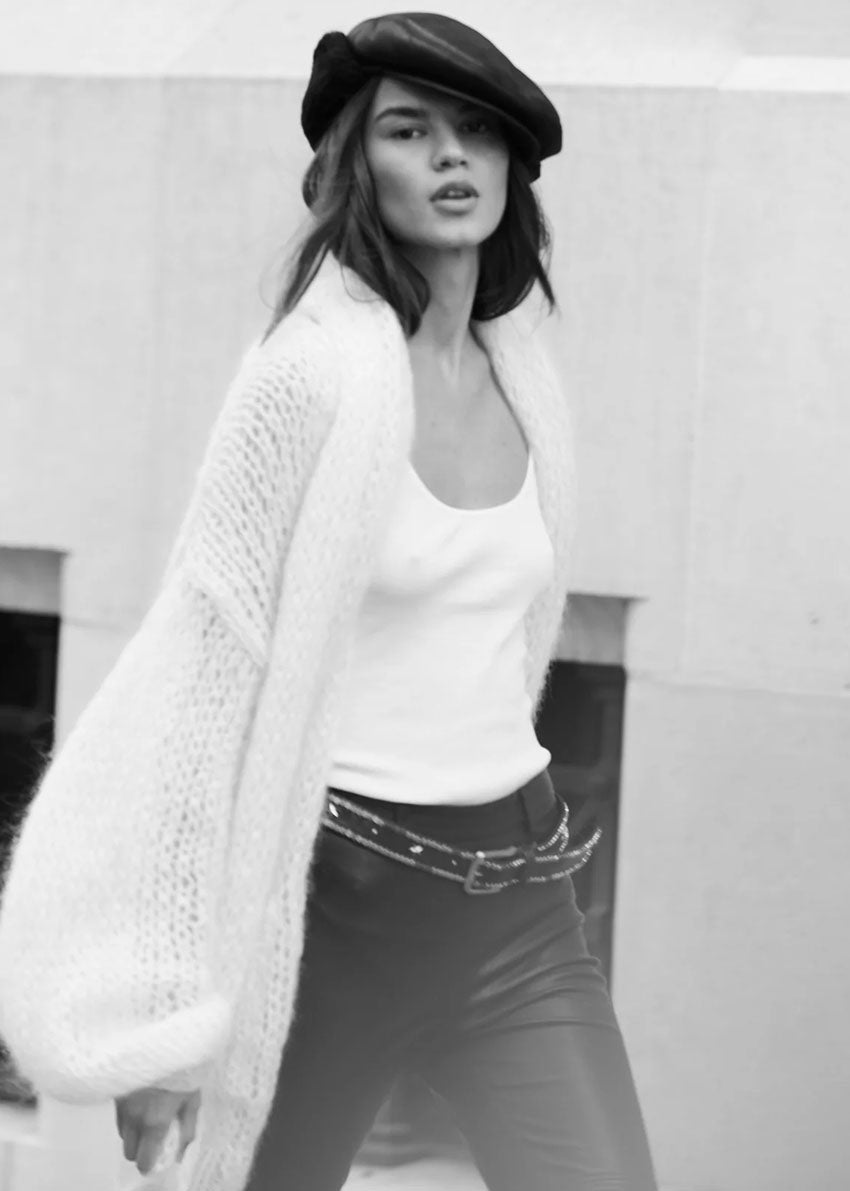 Black and white photo of a woman wearing a white cardigan, white top, and black pants.