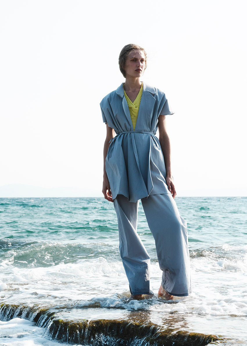 Person standing on a rock by the ocean wearing a light blue outfit.