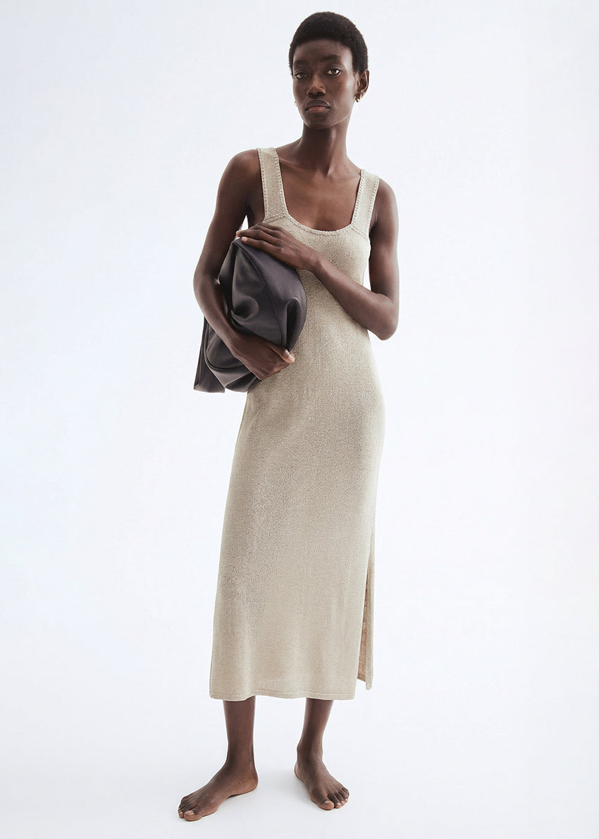 Woman wearing a beige sleeveless dress holding a gray towel against a white background