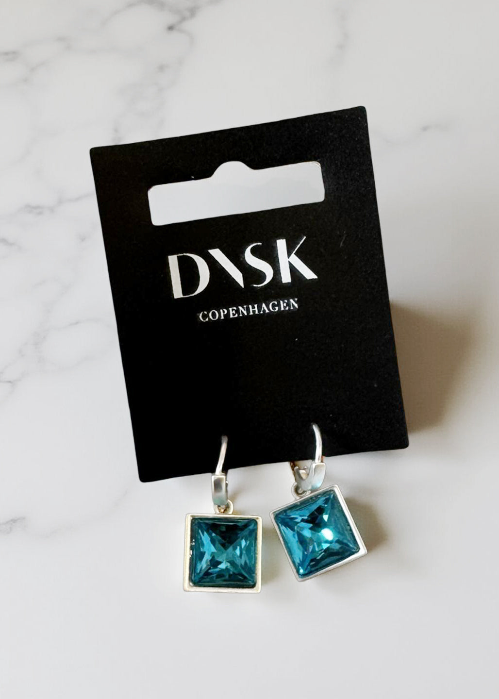 Blue square earrings on a Dansk Copenhagen card against a marble background