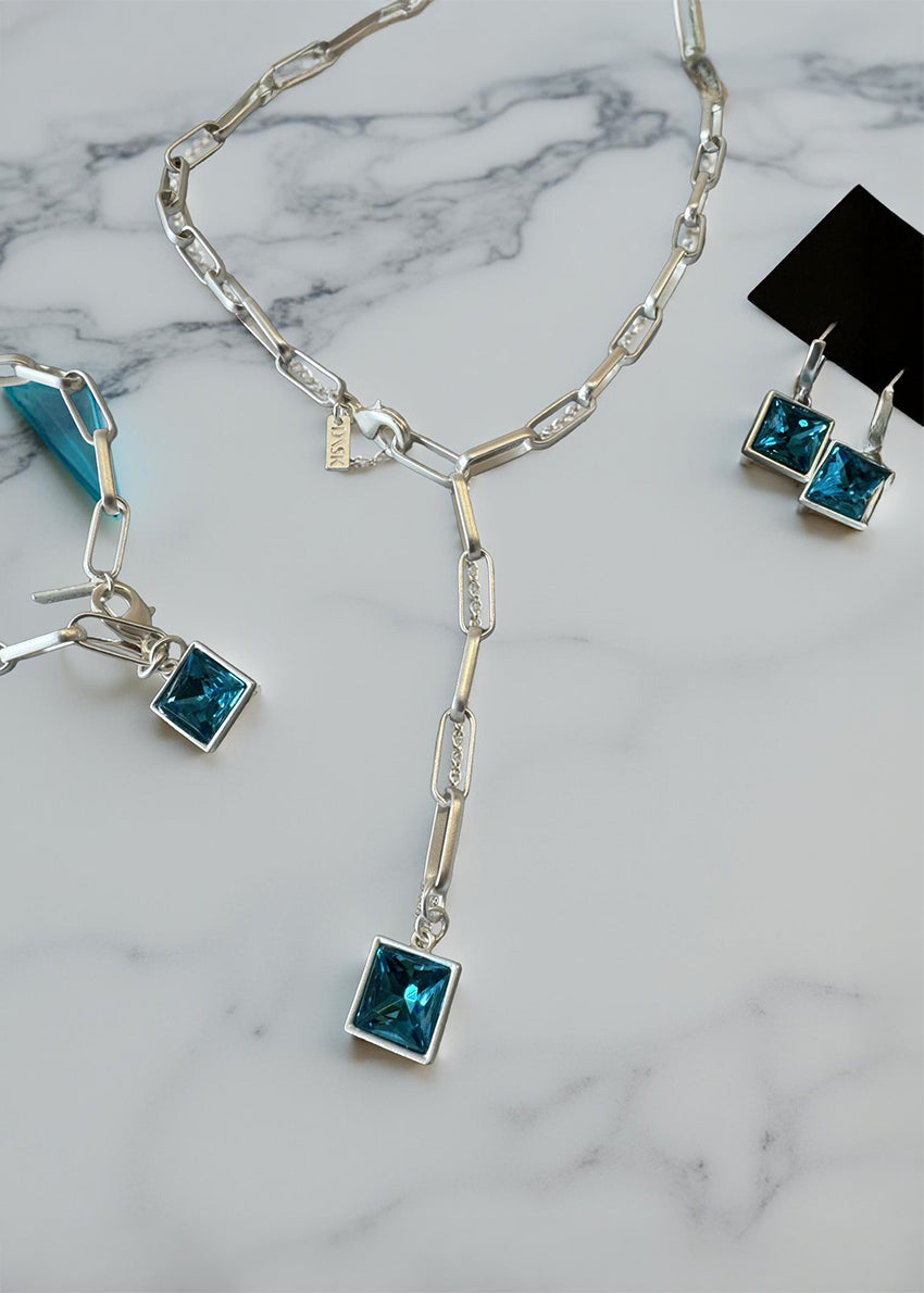 The centerpiece is a striking, square-cut blue gemstone pendant that catches the light beautifully, adding a pop of vibrant color and sophistication to any look