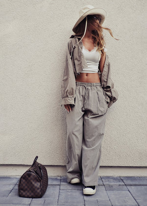 Person wearing a beige outfit with a white crop top and wide-leg pants, standing against a light gray wall.