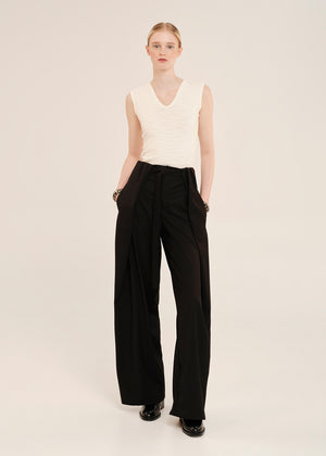 Woman wearing a white sleeveless top and black wide-leg pants on a plain background