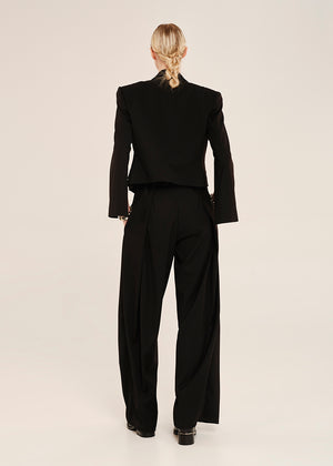 Person wearing a black suit standing against a plain background