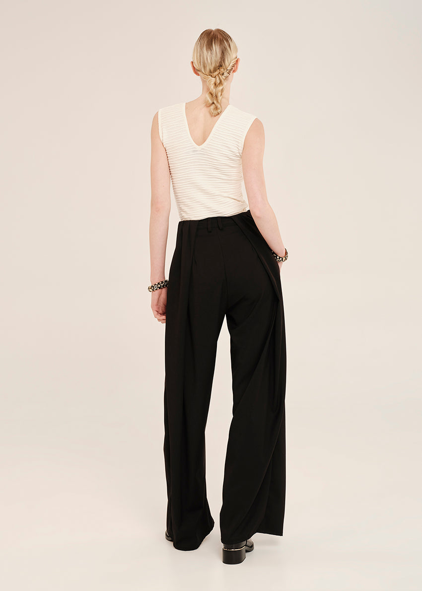 Person wearing a white sleeveless top and black wide-leg pants on a plain background