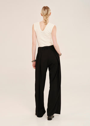 Person wearing a white sleeveless top and black wide-leg pants on a plain background
