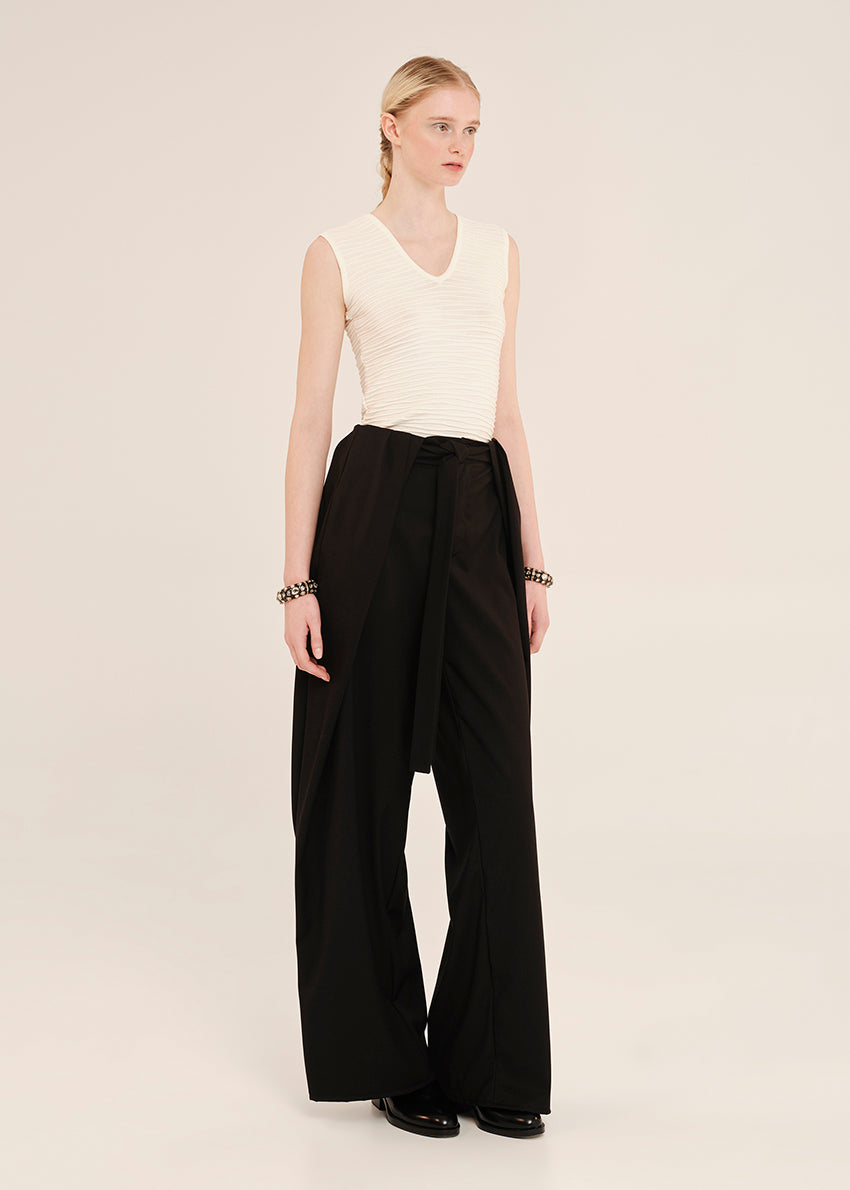 Woman wearing a white sleeveless top and black wide-leg pants on a plain background