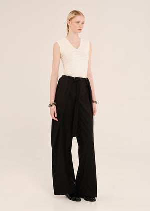 Woman wearing a white sleeveless top and black wide-leg pants on a plain background