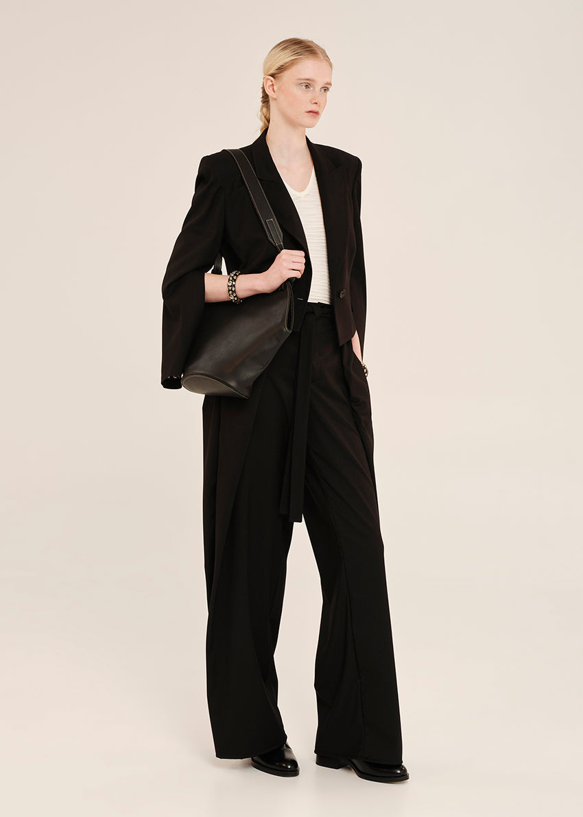 Woman wearing a black suit with a white shirt and holding a black bag on a beige background