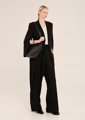 Woman wearing a black suit with a white shirt and holding a black bag on a beige background