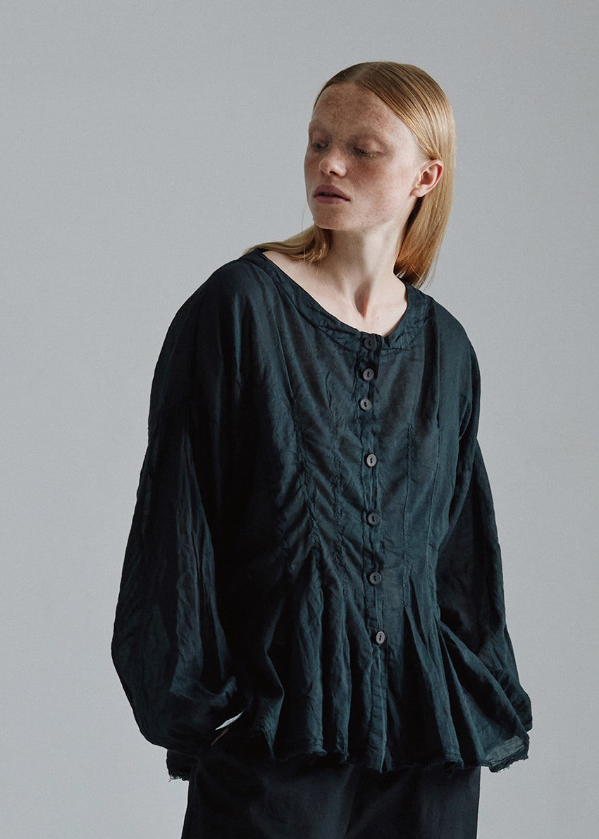 A model wearing a long-sleeved, waisted loose-fit black shirt with bottom pleats.