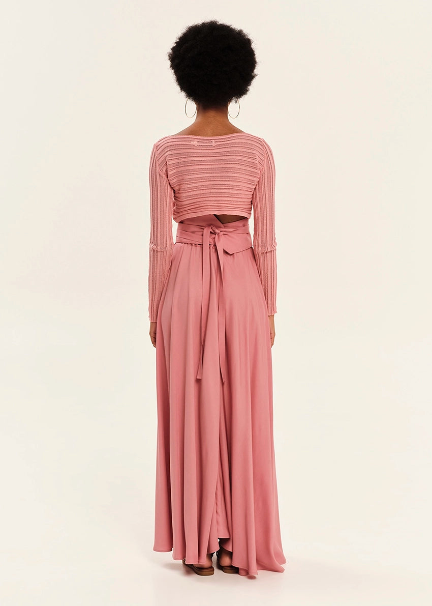 Person wearing a pink long-sleeve top and flowing skirt set on a white background