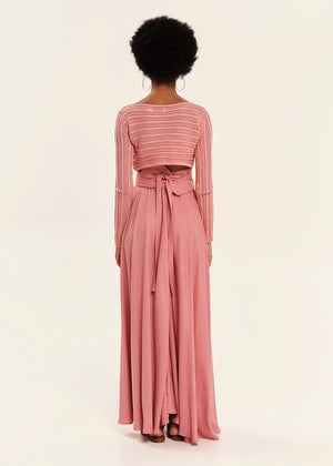 Person wearing a pink long-sleeve top and flowing skirt set on a white background
