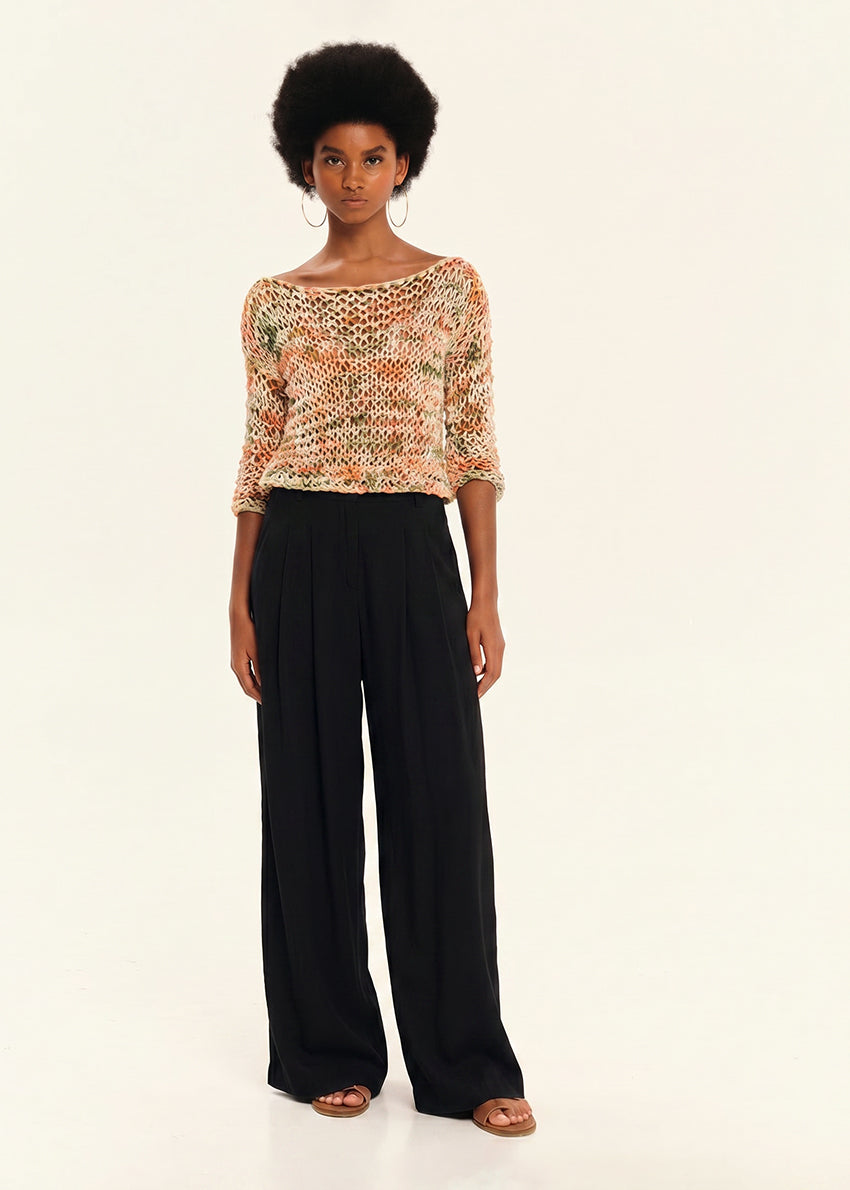 Woman wearing a patterned top and black pants on a white background