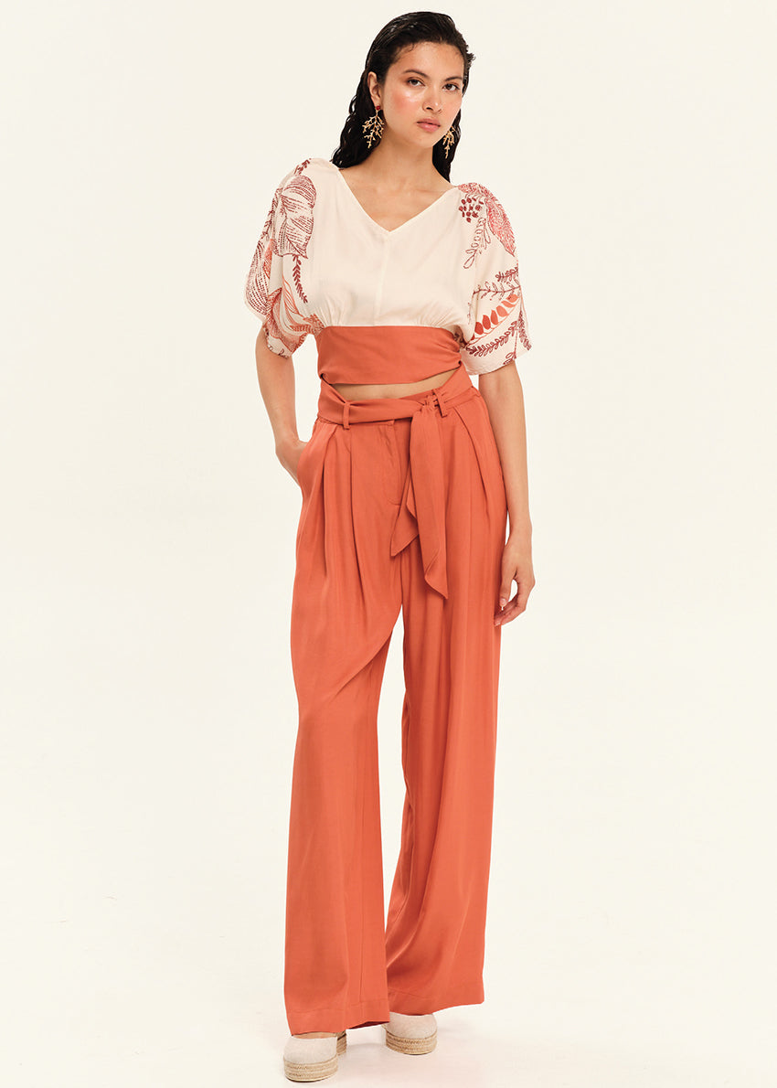 Woman wearing a orange outfit with a white top and wide-leg pants on a light beige background