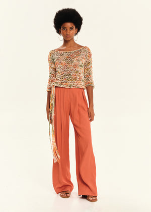 Woman wearing a orange outfit with a white top and wide-leg pants on a light beige background