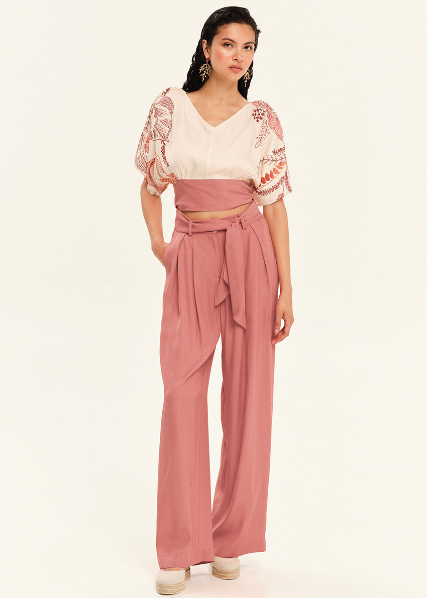 Woman wearing a patterned top and black pants on a white background
