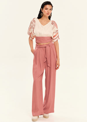 Woman wearing a pink outfit with a white top and wide-leg pants on a light beige background