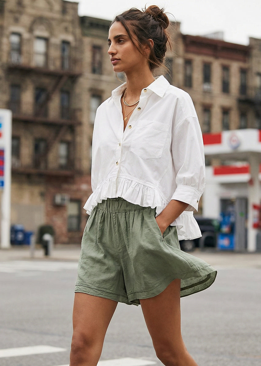 Woman wearing a white blouse and green shorts on a city street.