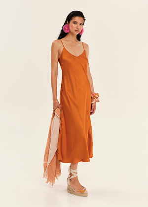 Woman wearing an orange slip dress with a beige scarf on a white background