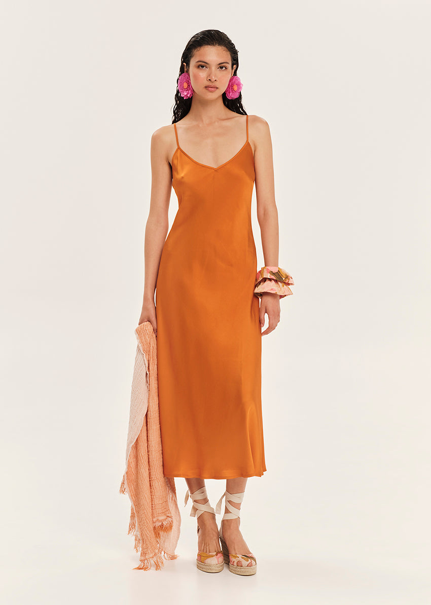 Woman wearing an orange slip dress with a plain background