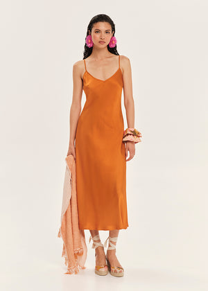 Woman wearing an orange slip dress with a plain background