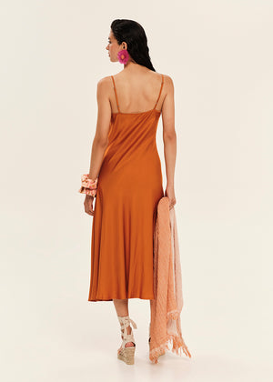 Woman wearing a rust-colored slip dress with a sheer orange scarf on a white background