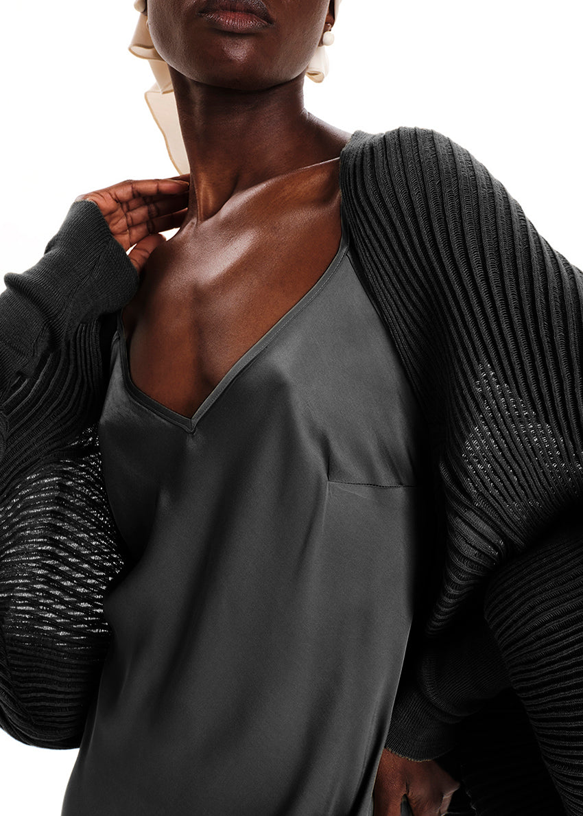 Person wearing a dark gray dress with a textured black cardigan on a white background