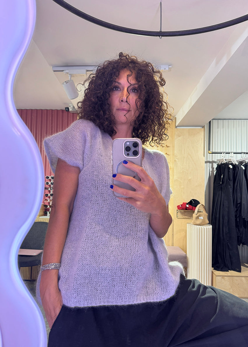 Person taking a mirror selfie wearing a light gray sweater in a room with clothing racks.