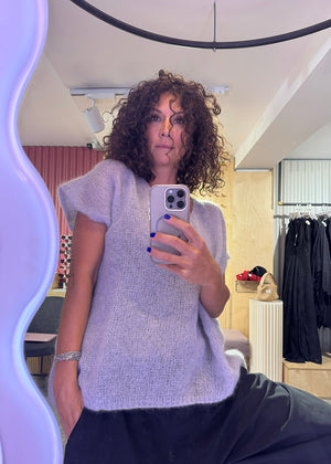 Person taking a mirror selfie wearing a light gray sweater in a room with clothing racks.