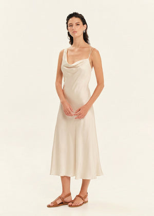Woman wearing a beige slip dress against a plain background