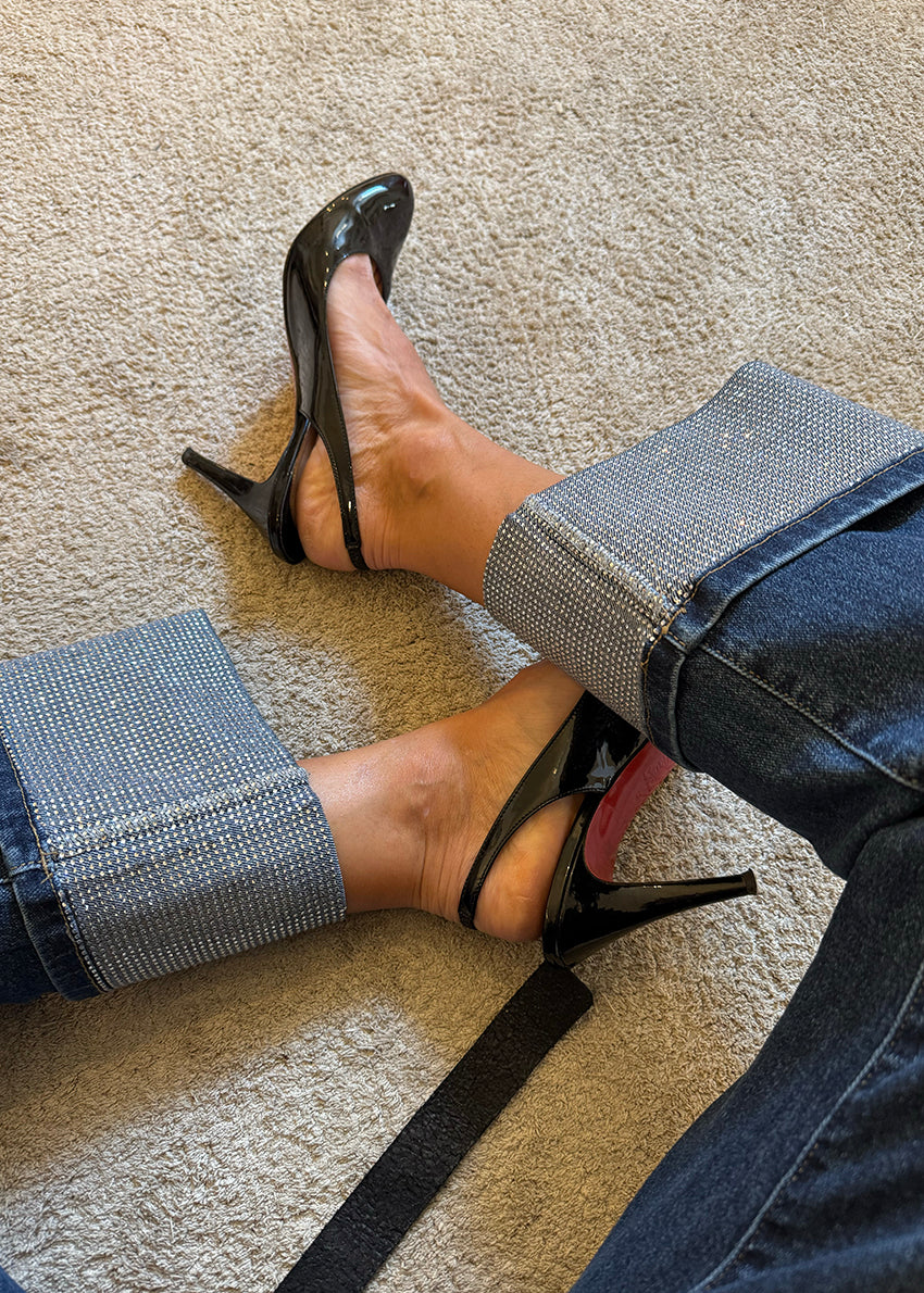 Person wearing black high-heeled shoes and blue jeans with sparkle cuff on a beige carpet.